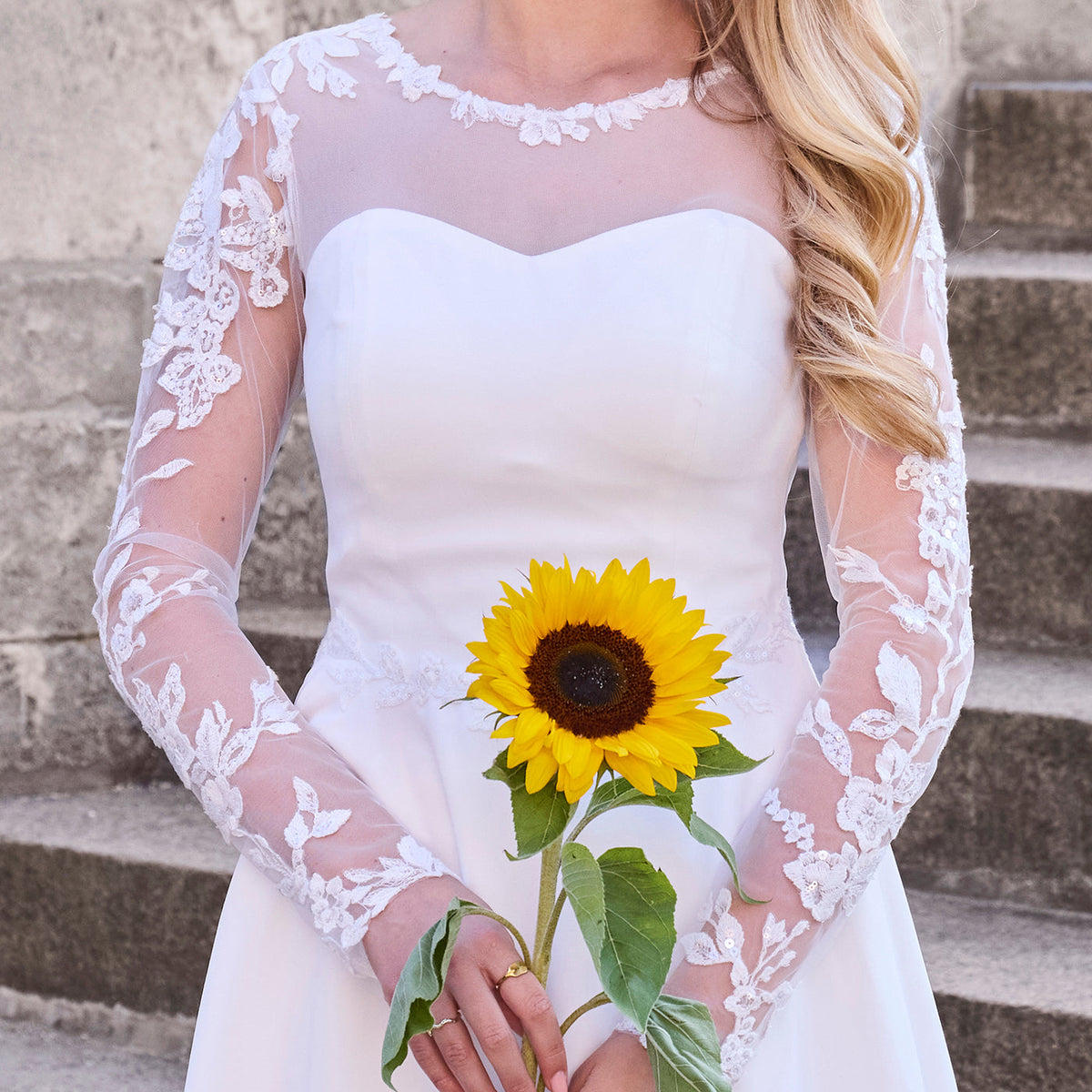 pige står med solsikke i hånden og  viser konfirmationskjole i chiffon, med blomsterdetaljer med lidt glitter på ærmer og rundt i halsen. 